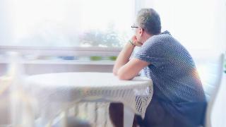 A man sitting at a table alone, resting his chin in his hand, looking out a window.
