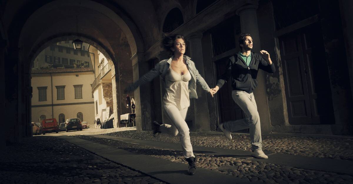 A couple holding hands as they run down an alleyway.