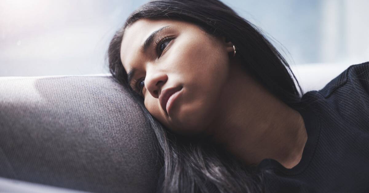 A woman leaning her head against the back of her couch, looking dejected.