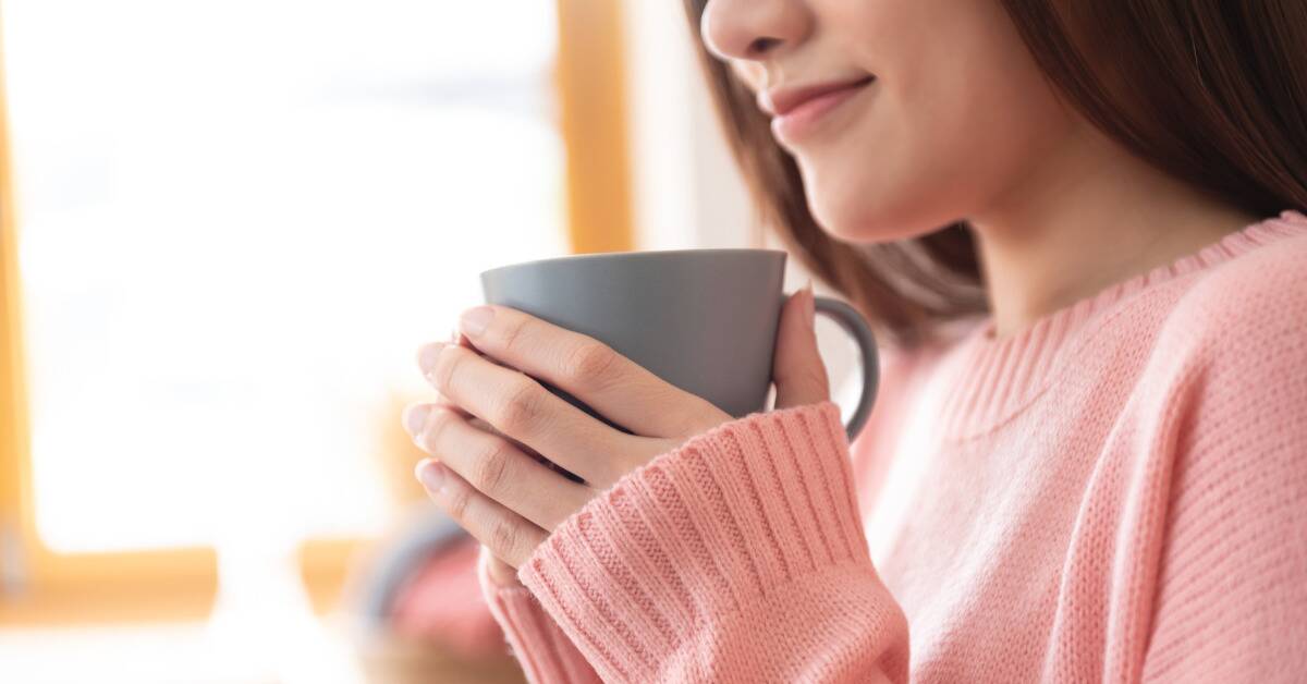 A woman in a  pink sweater cradling a mug in both her hands.