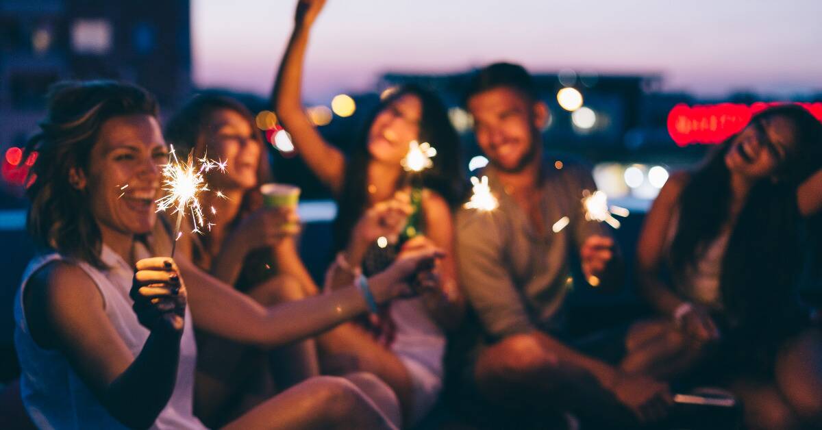 A group of friends sitting on a building rooftop with sparklers, celebrating something.