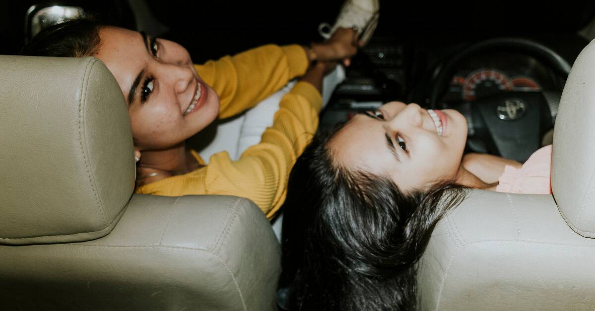 Two friends sitting in the front seats of a car, leaning back and smiling so someone in the back seat can take a photo of them both.