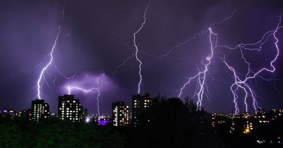 A city skyline with multiple bolts of purple tinted lightning striking throughout.