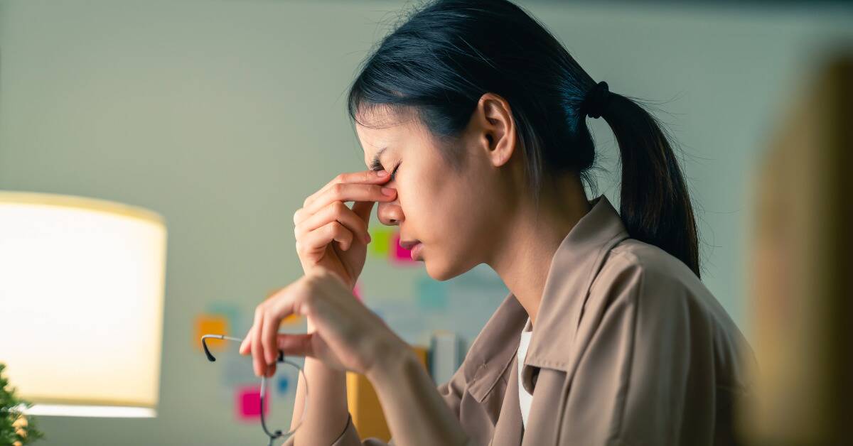 A woman looking stressed, pinching the bridge of her nose.