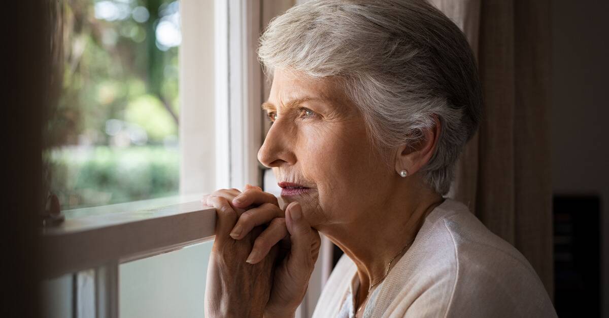 A woman stood close to the window, hands on the frame, looking out pensively.