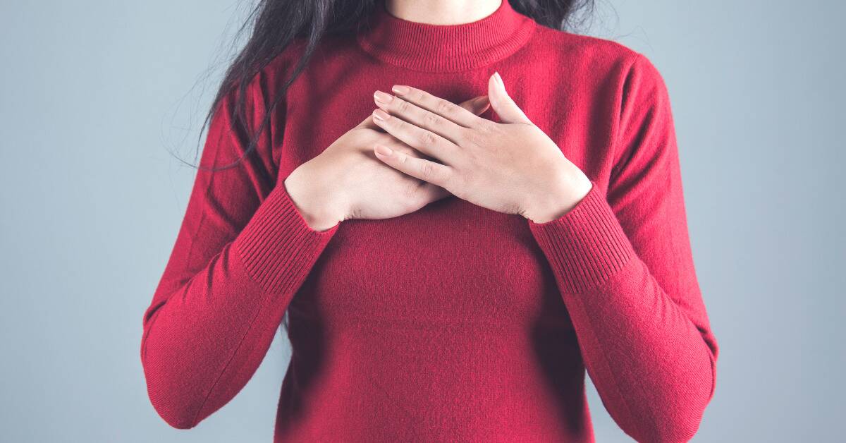 A woman in a red sweater with her hands over her heart.
