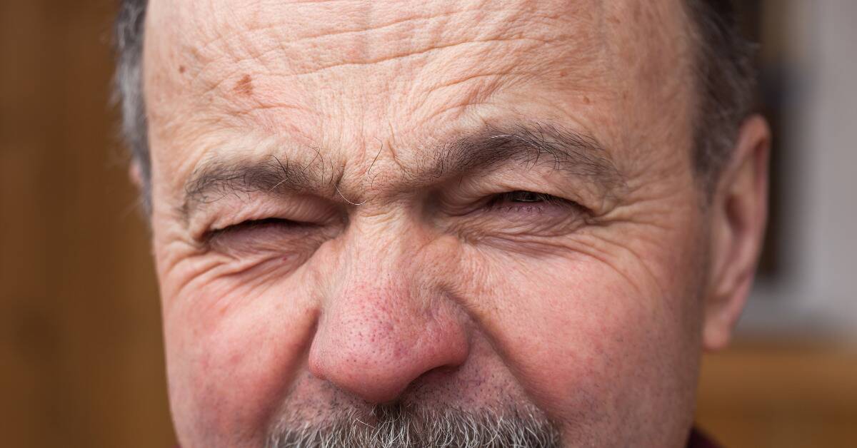 A closeup of an older man's forehead as he's squinting, a small mark on his skin.