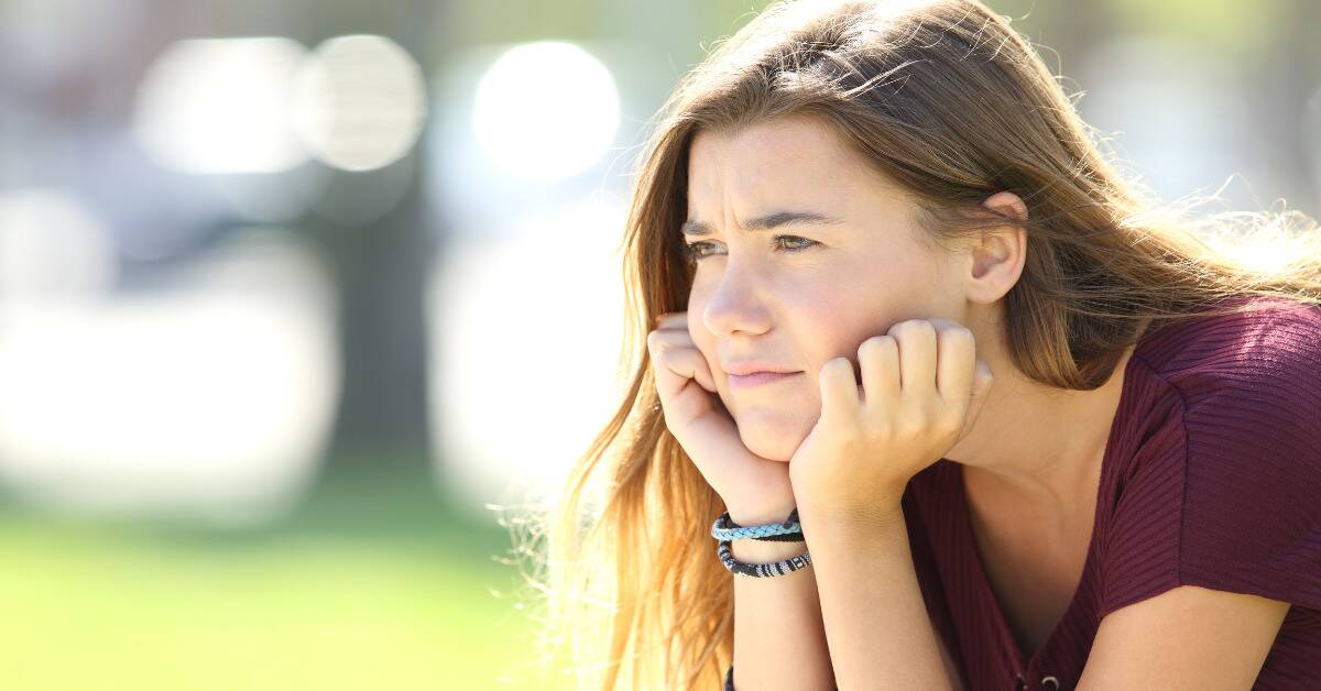 A teenage girl looking sad, resting her chin in her hands.