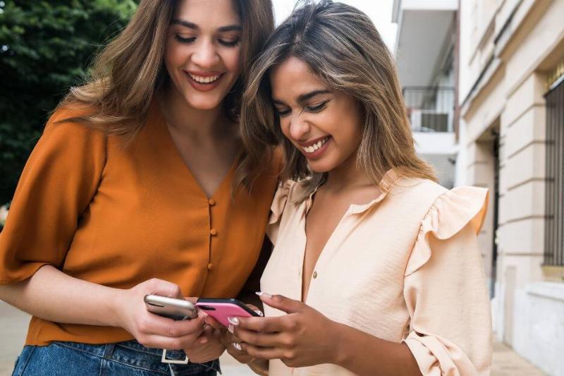 Two women looking down at their smartphones and smiling.