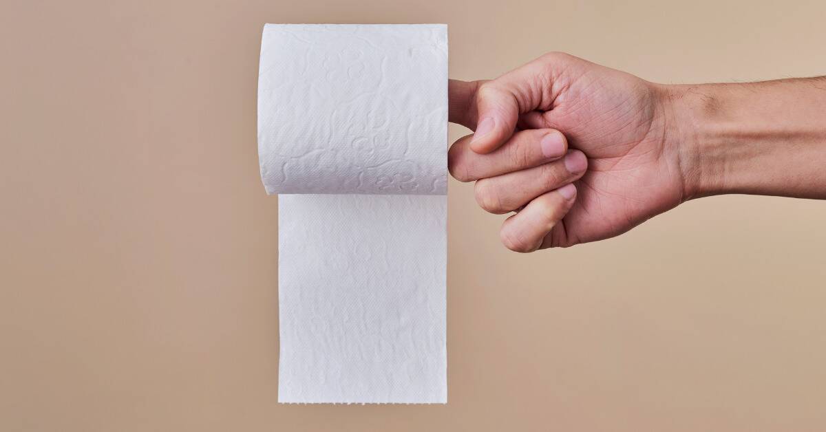 Someone holding out their hand, one finger extended, a toilet paper roll placed on it, against a beige background.