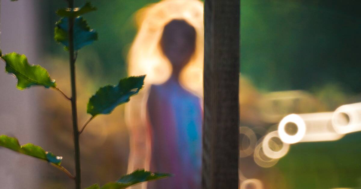 A blurry photo of someone through a window, a glowing aura around them.