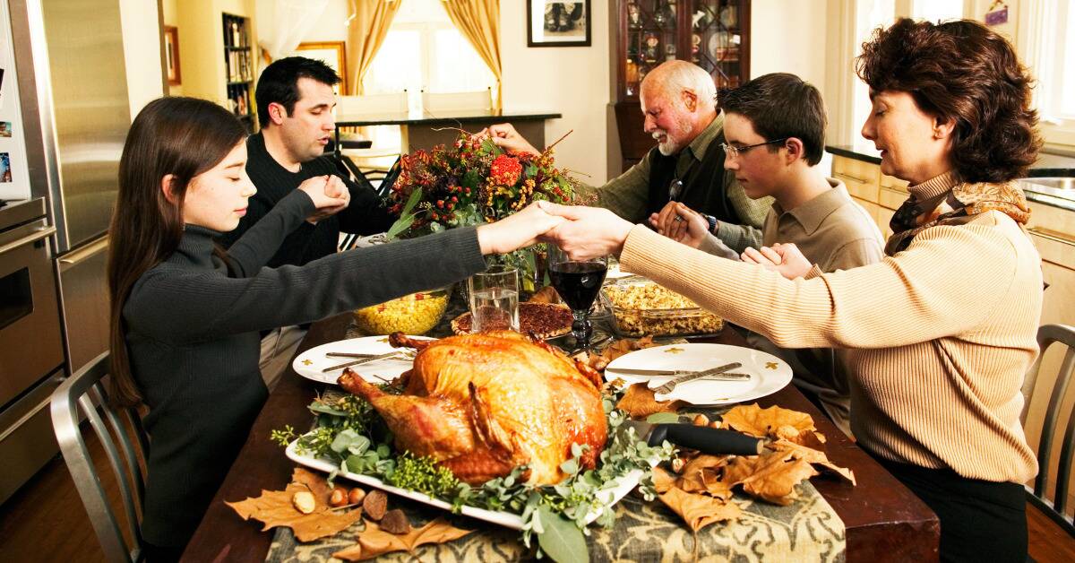 A family holding hands and saying grace at a Thanksgiving dinner table.