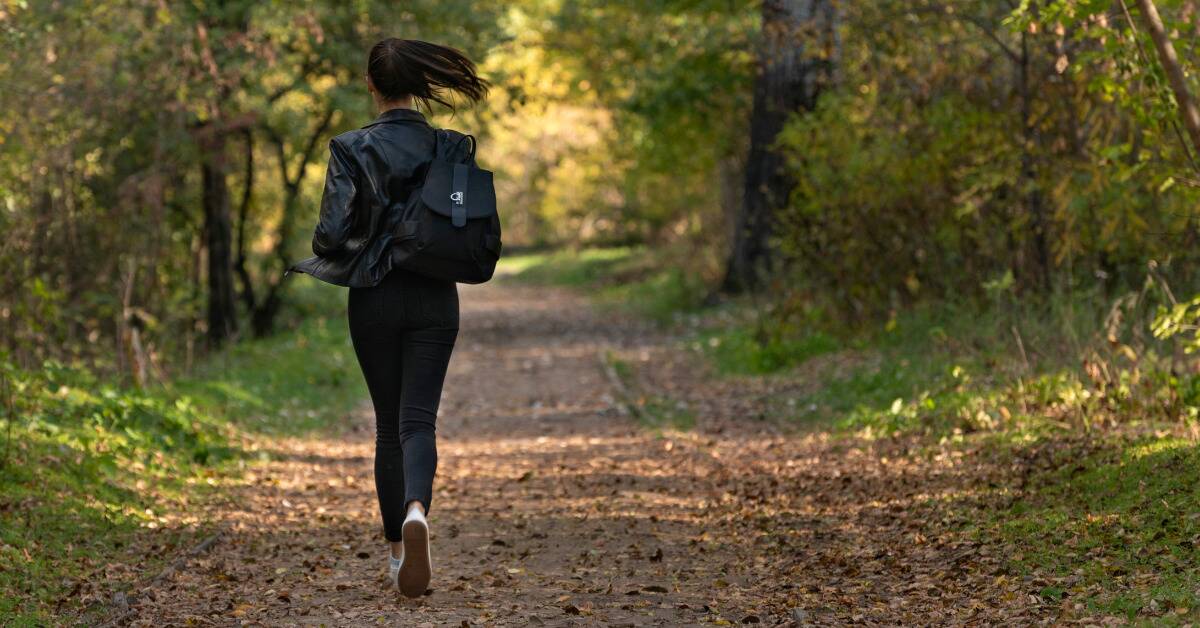 A woman in all black lightly jogging down a path, away from the camera.