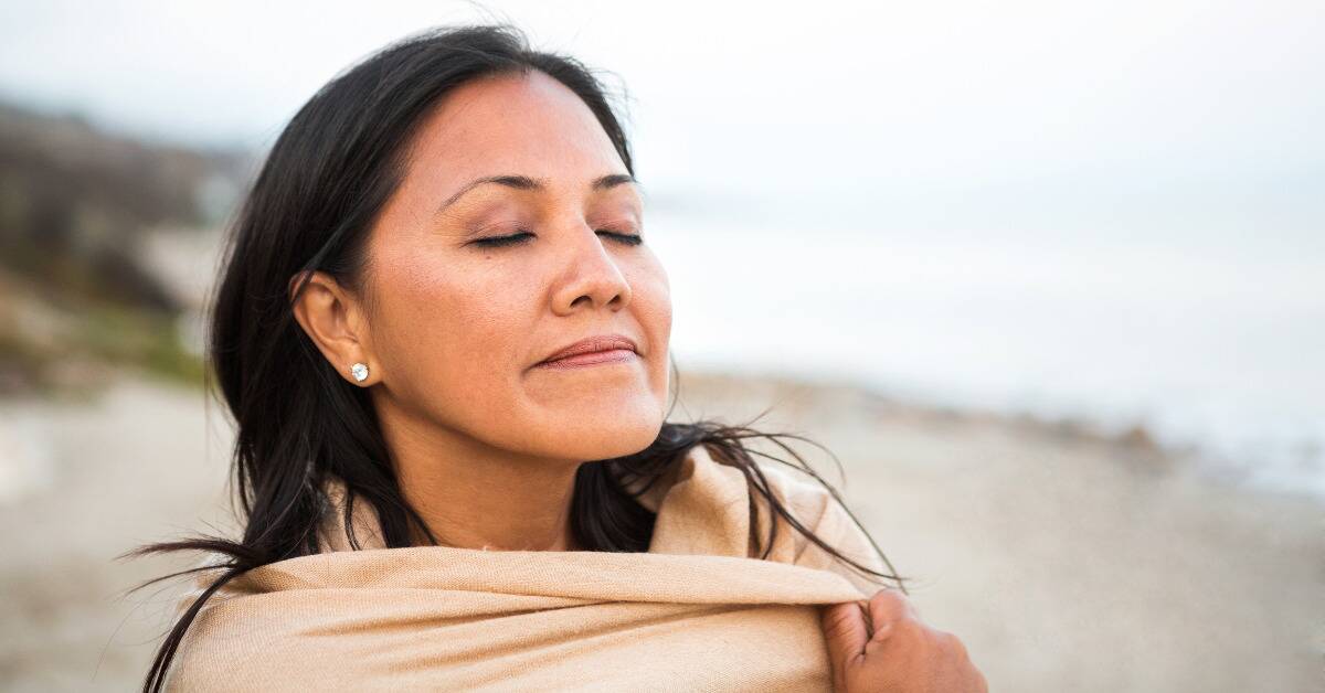 A woman smiling peacefully outside, a blanket wrapped around her shoulders.