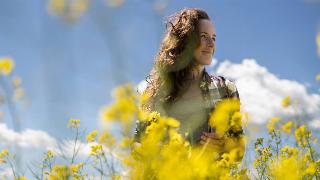 A low shot of a woman smiling as she walks through a field of yellow flowers.