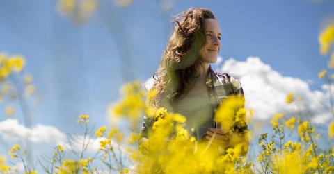 A low shot of a woman smiling as she walks through a field of yellow flowers.