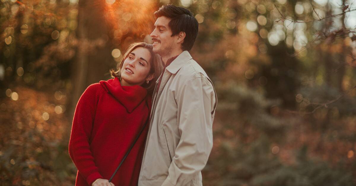 A couple is out in nature, the woman leaning into the man as they both look at something.