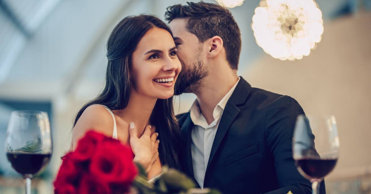 A couple on a date, the man leaning in to kiss the woman's cheek while the woman smiles.