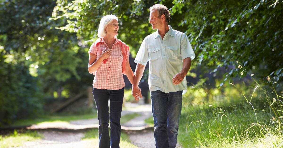 A couple walking down a path in nature, holding hands and smiling as they talk.