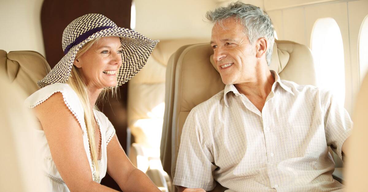 A couple seated next to each other, the woman smiling as she looks out the window, the man smiling looking at her.