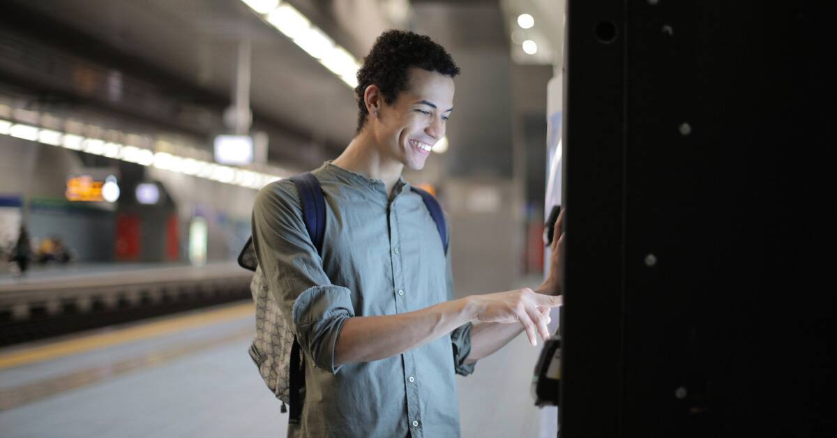 A man is smiling as he uses a public transit terminal.