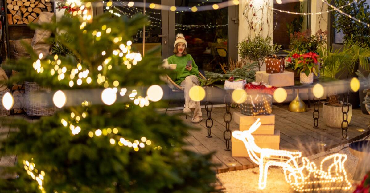 A woman smiling as she's sat outside in a yard decorated with Christmas decorations.