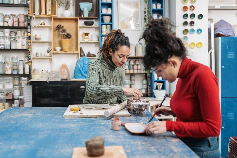 two women in sweaters seated in art class painting