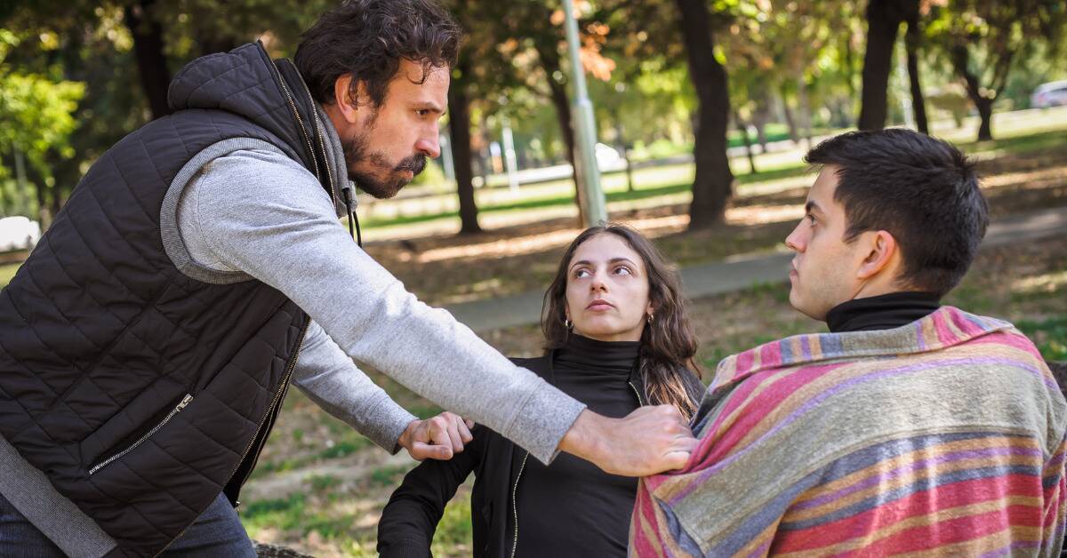 A man pulling another man and a woman apart, looking angry.