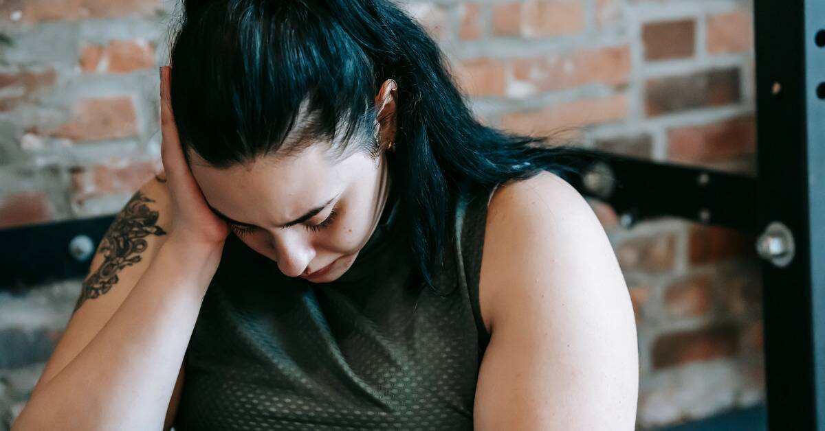 A woman looking down at herself, seeming ashamed, her head resting in her hand.