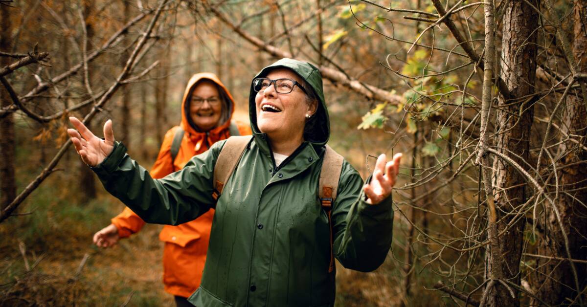 Two friends smiling as they hike through a forest in their raincoats.