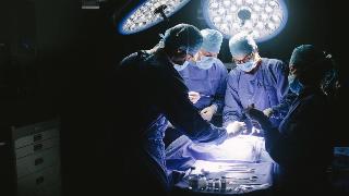 A group of surgeons lit only by bright surgery lights circled around a patient they're about to operate on.