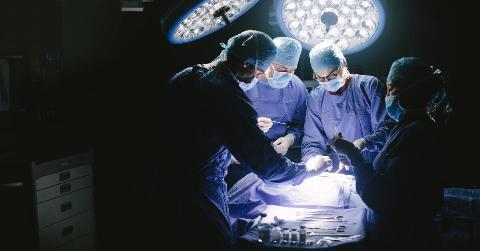 A group of surgeons lit only by bright surgery lights circled around a patient they're about to operate on.