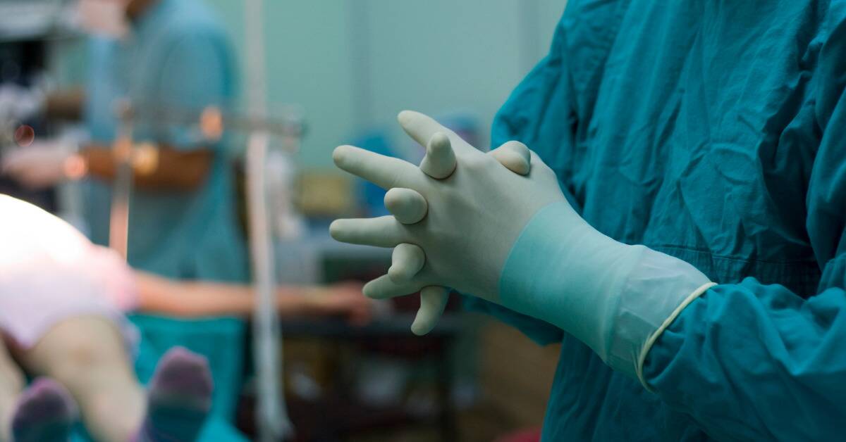 A close shot of a surgeon's gloved hands with their fingers interlocked together.