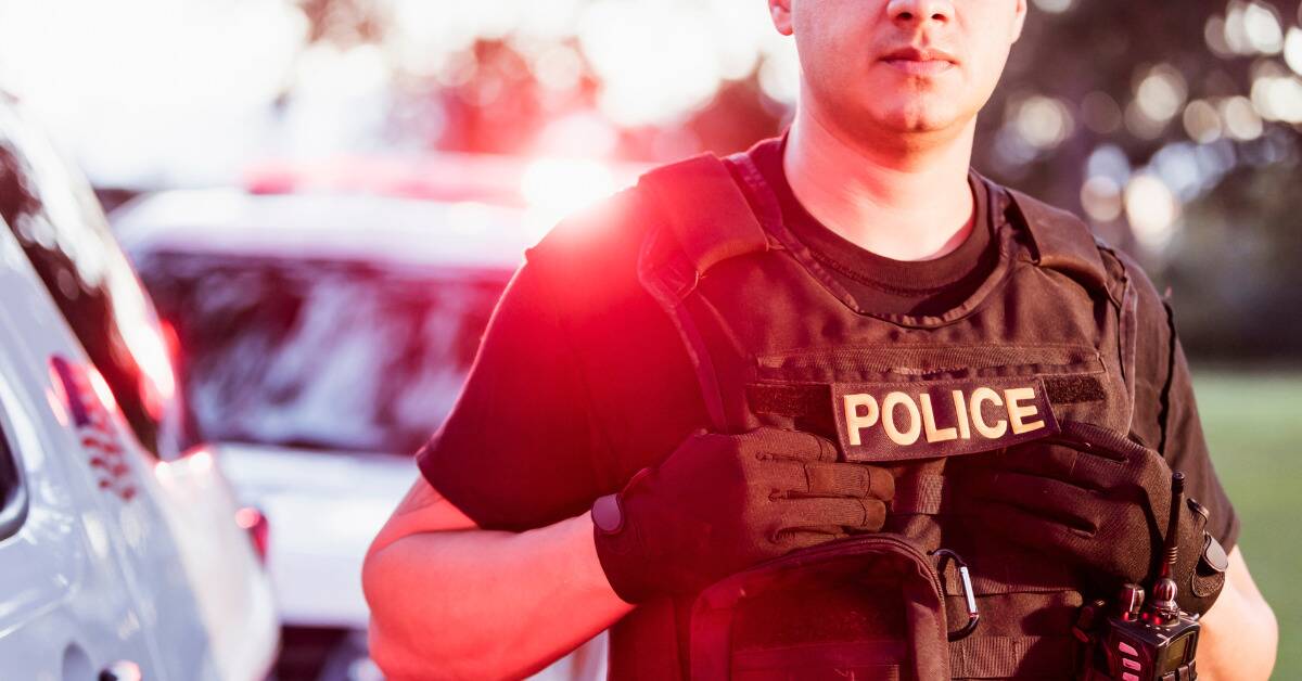 A close shot of a police officer holding onto his vest under a badge that says 