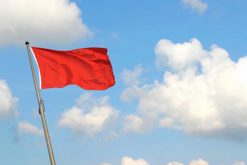 A red flag raised against a sky background.