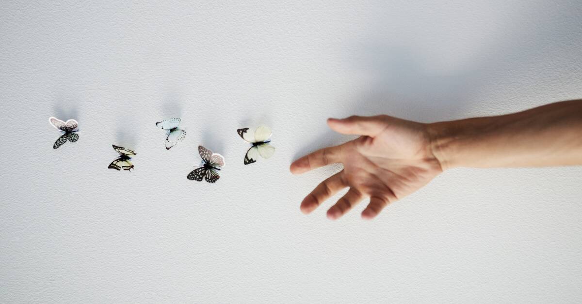 A posed photo of a hand letting go of some small butterflies.
