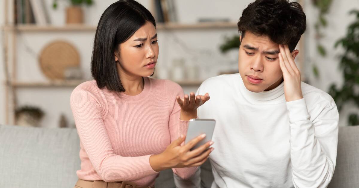 A woman showing a man a phone, looking confused, while the man looks stressed.