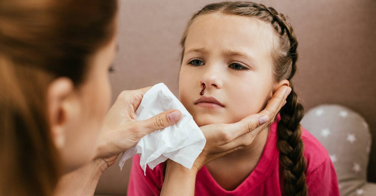 A little girl having a nosebleed, a woman holding a tissue close to her face.