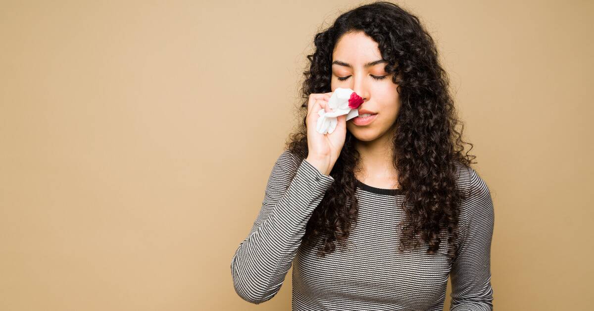 A woman holding a now-bloody tissue to her nose.