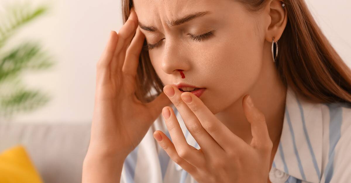 A woman experiencing a nosebleed, her hand to her temple.