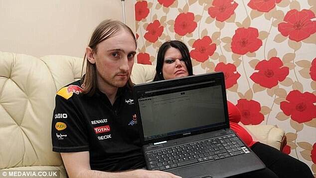 Steve and Debbie sitting on a couch next to each other, both looking at the camera, Steve holding up his laptop.