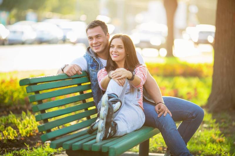Young couple on a park on a bench smiling.