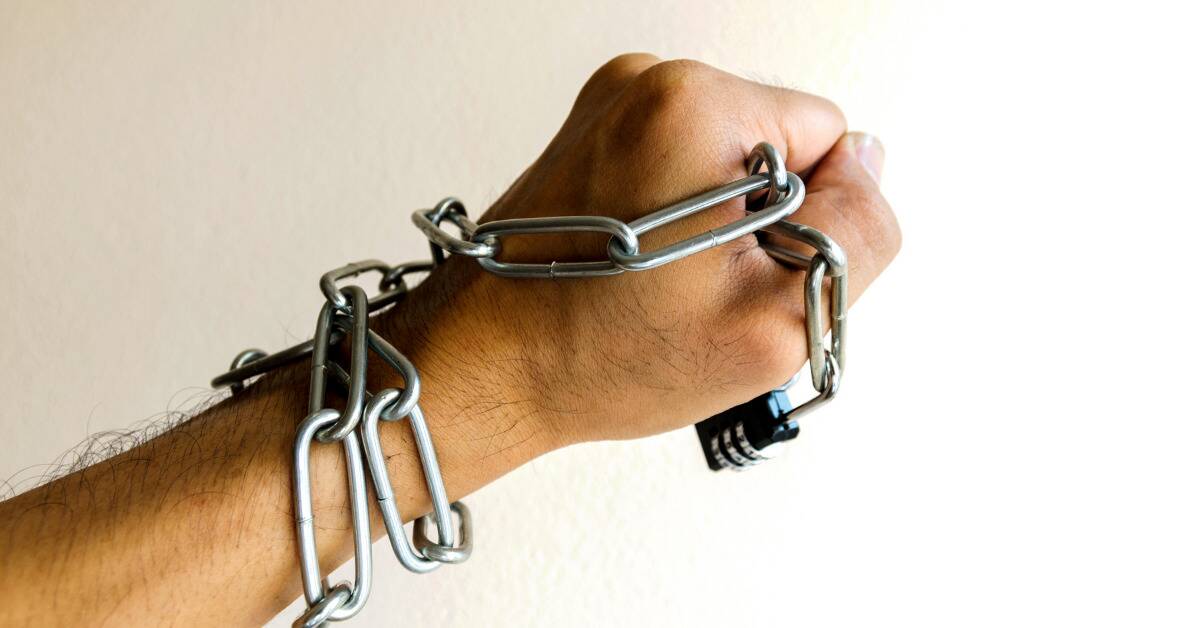 A hand held in a fist, a chain and lock wrapped around it, going up the person's arm.