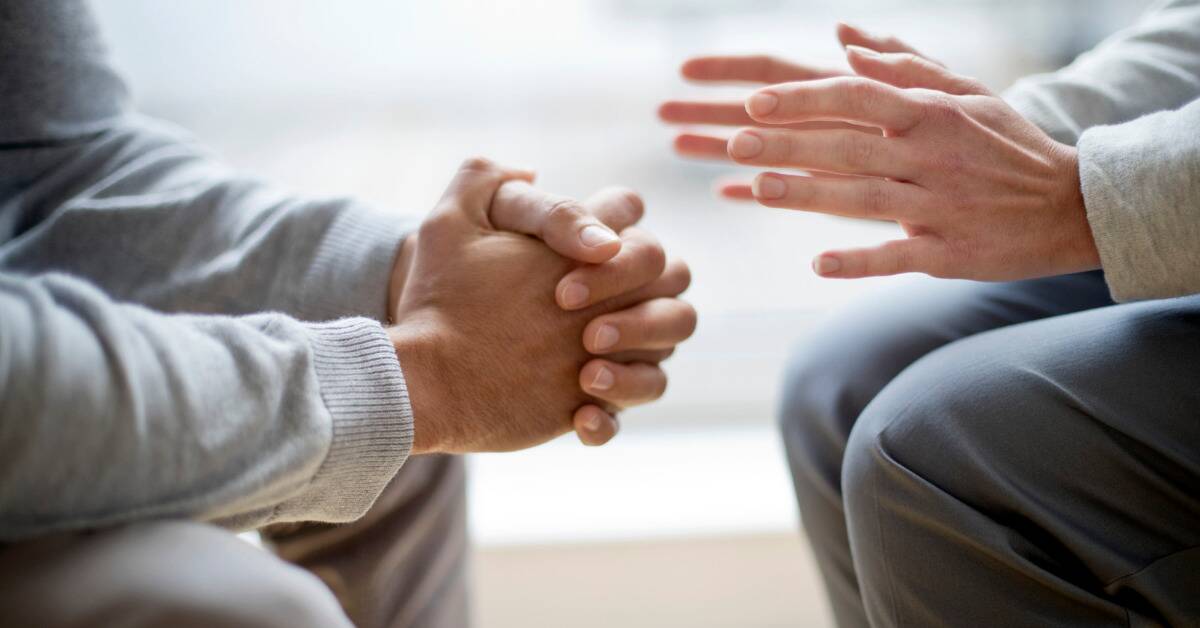 A closeup of the hands of two people talking, one person having both hands folded together with the other out as they speak.
