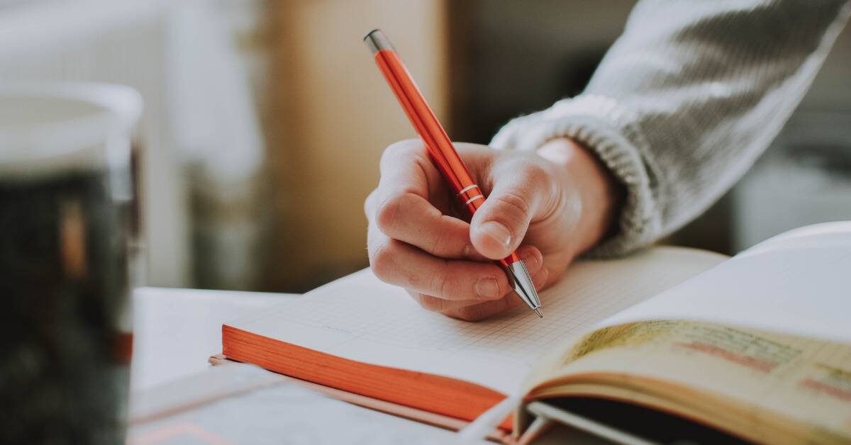 A hand holding an orange metal pen, about to start writing in a notebook.