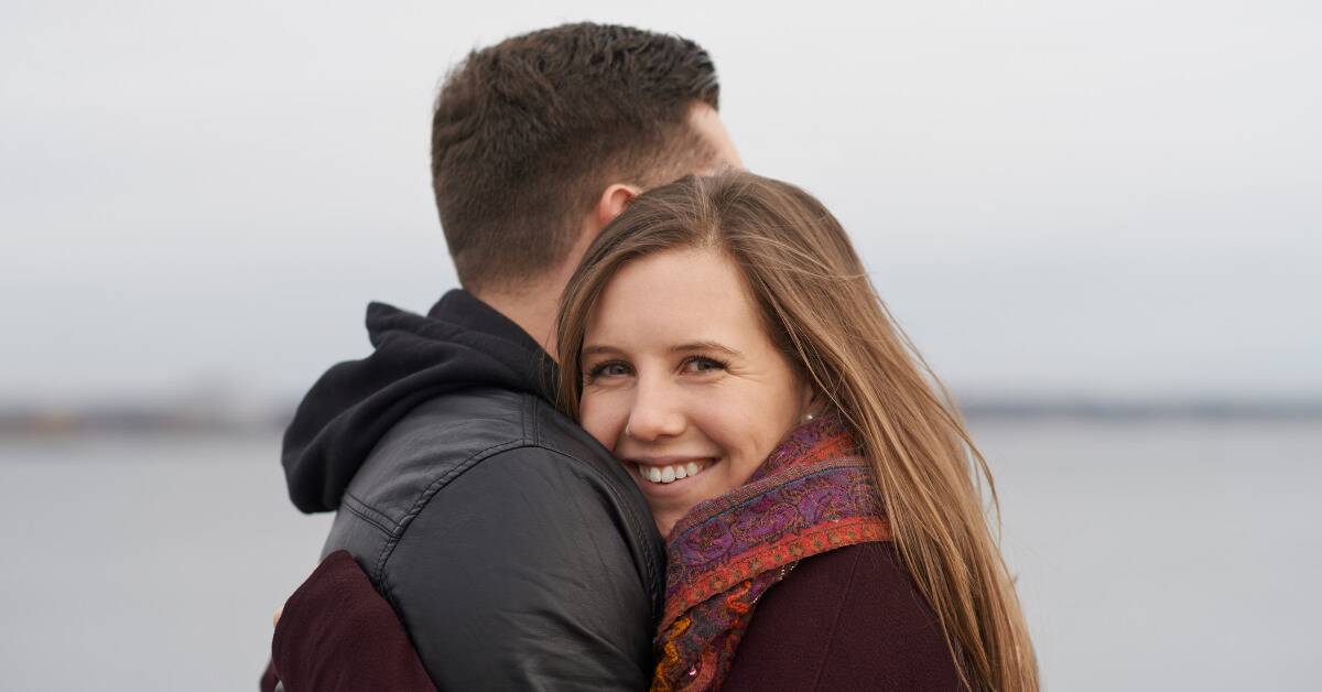 A couple hugging, the woman smiling and looking at the camera.