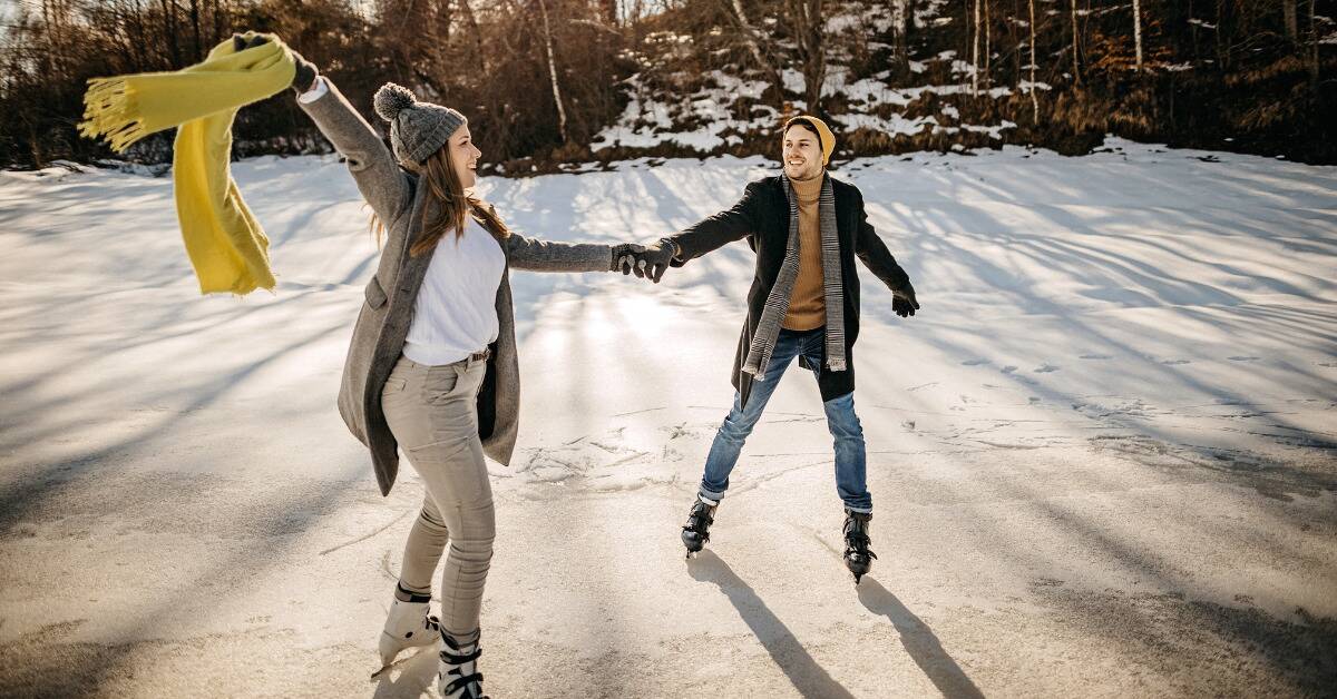A couple ice skating together, holding hands, the woman waving her scarf around.