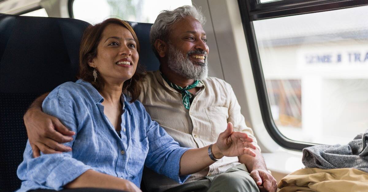 A couple sitting next to each other on public transit, the man with an arm around the woman who's leaning into his side.