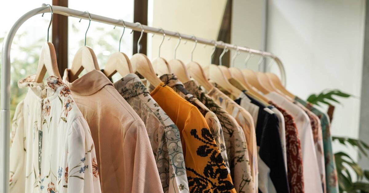 A rack of a closet holding a variety of light, colorful, patterned shirts on wooden hangers.