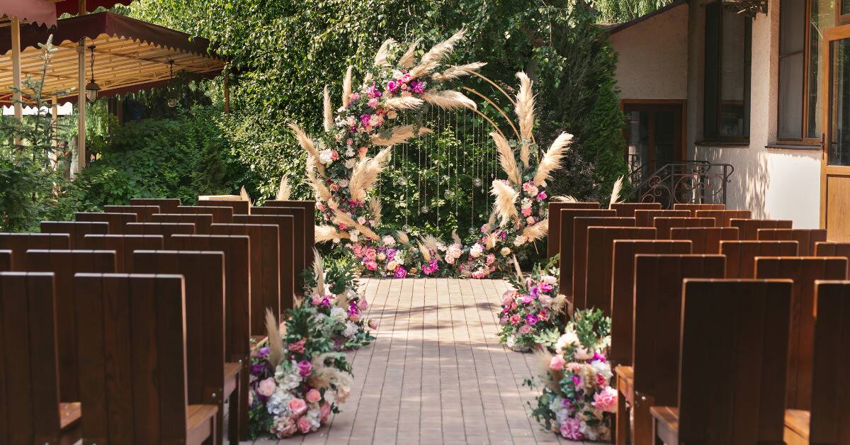 A look down the aisle at a wedding arch, aa circular one adorned with flowers and reeds.
